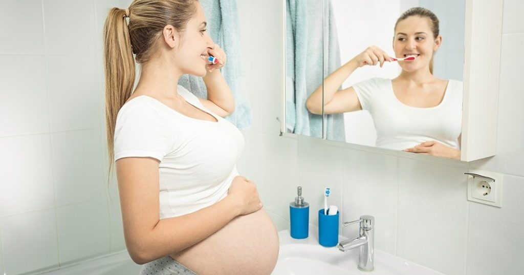 Mujer embarazada mirandose al espejo y cepillándose los dientes